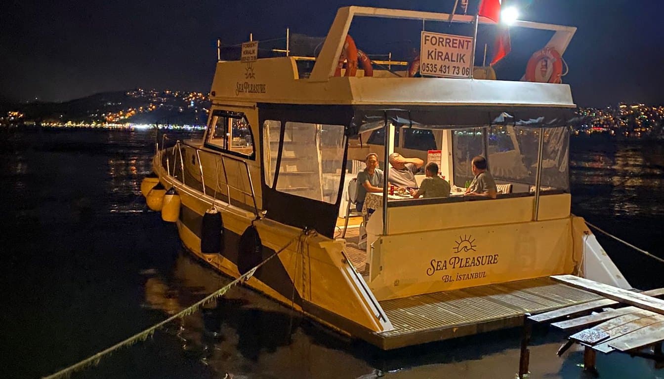 İstanbul Boğazı'nda gün batımında ilerleyen, açık güverteli, maksimum 10 kişilik butik özel yat; arka planda Boğaz yalıları ve köprü