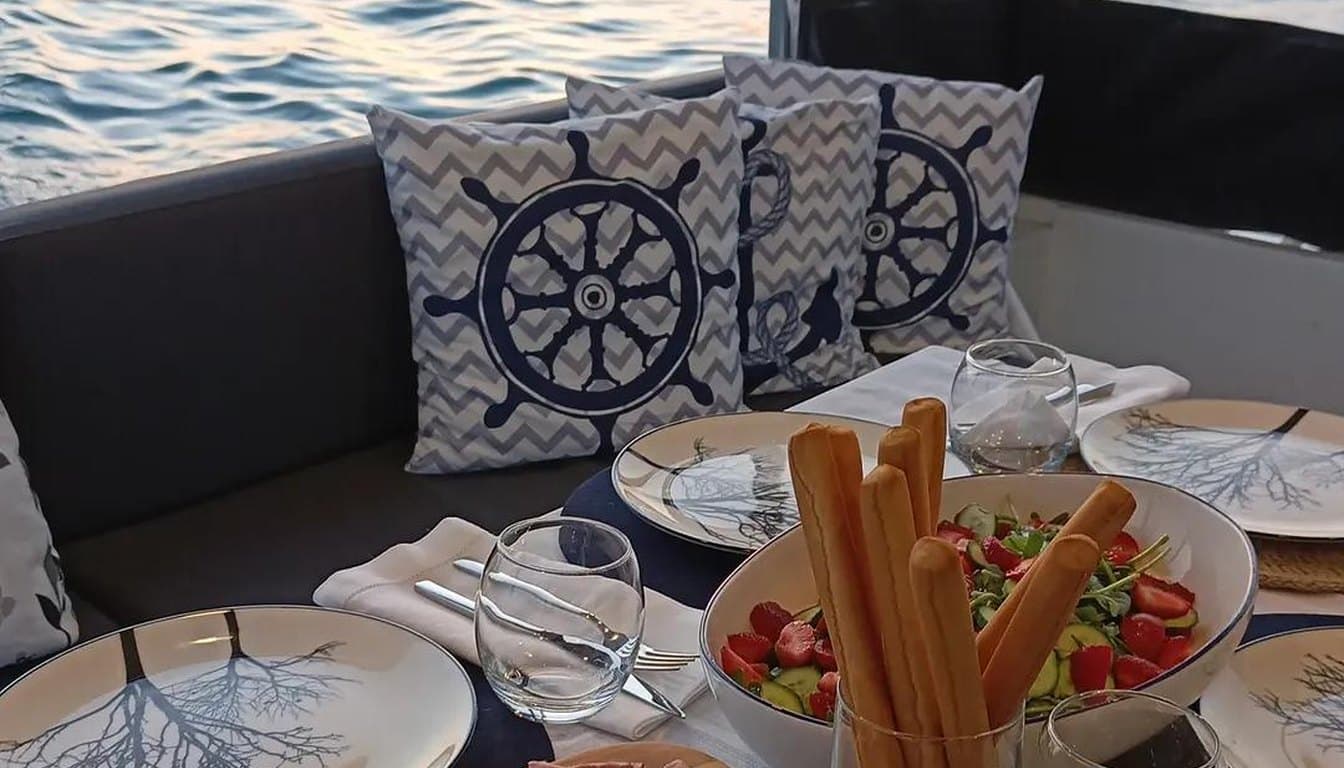 İstanbul Boğazı'nda küçük, butik bir teknenin güvertesinde çay bardakları, çiçekler ve sıcak ışıklarla hazırlanmış samimi bir sürpriz kutlama düzeni, gün batımı ışığı.